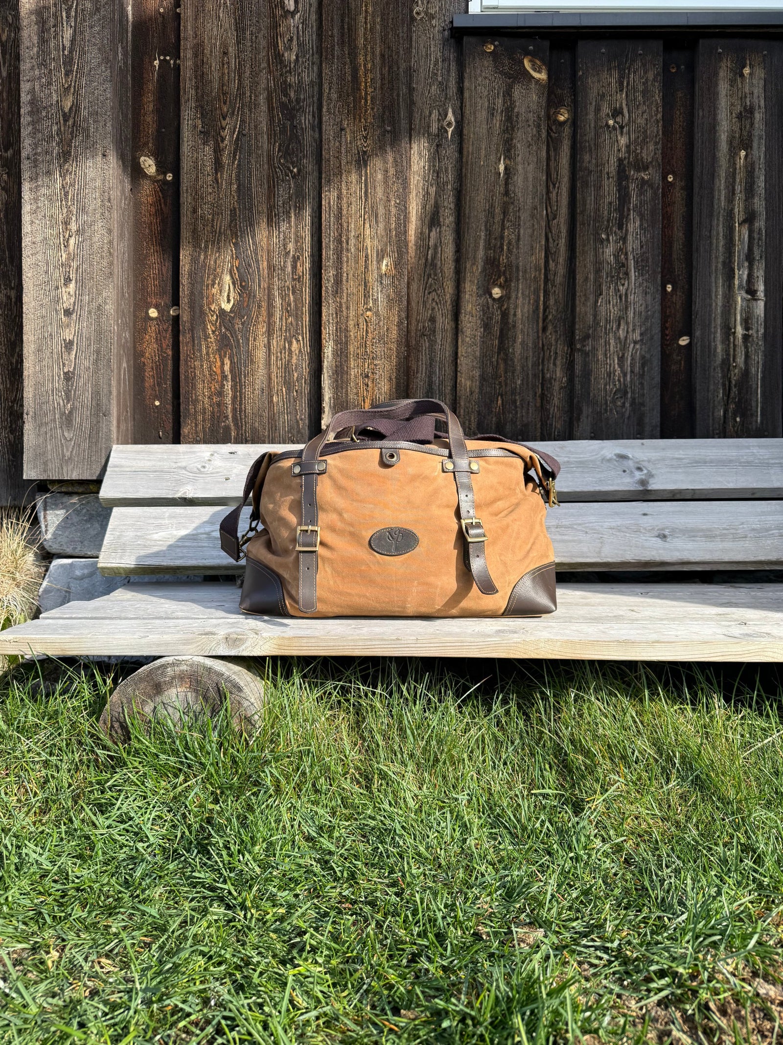Fara duffelbag i lys brun vokset canvas på en gammel trebenk foran en tømmervegg