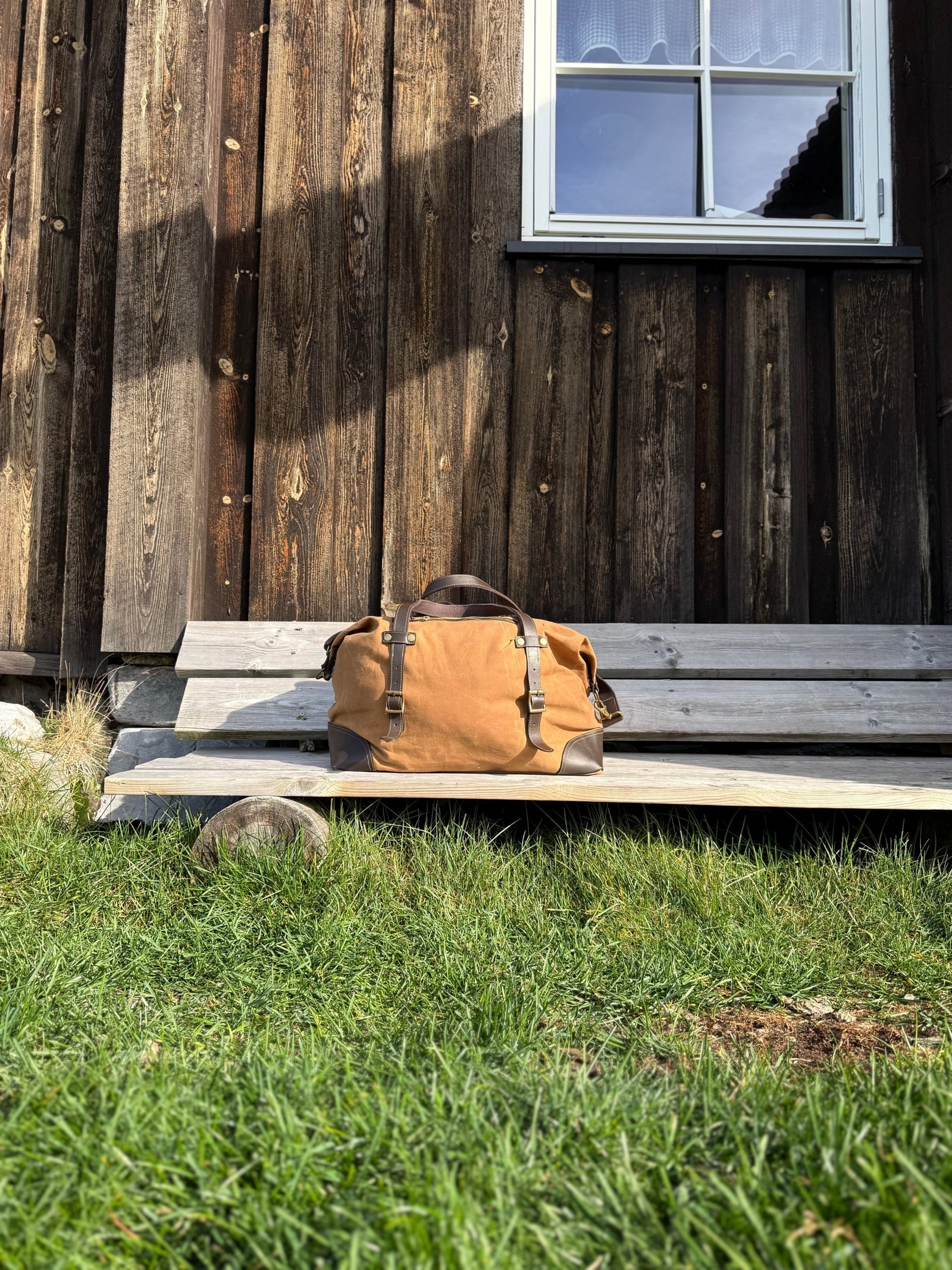 Fara duffelbag på en trebenk utenfor en hytte, med gress i forgrunnen